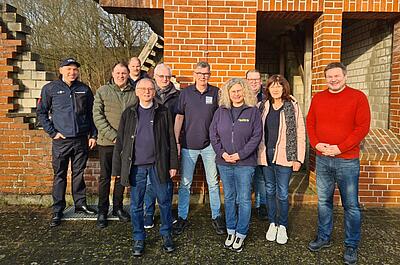 Eine Gruppe Menschen steht vor einem Trümmerhaus.